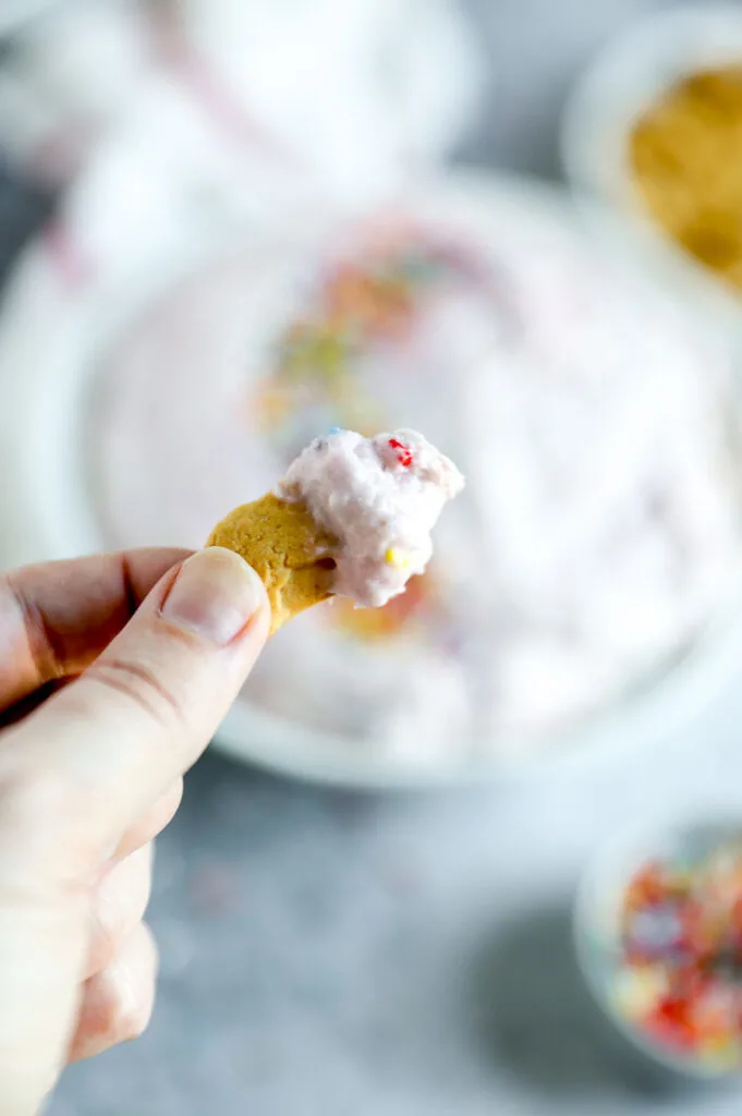 a hand holding an animal cracker with dunkaroo dip