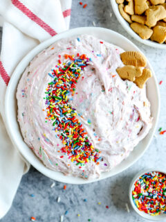 a white bowl with dunkaroo dip covered in sprinkles next to a bowl of animal crackers