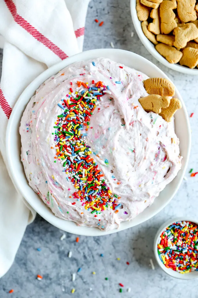 a white bowl with dunkaroo dip covered in sprinkles next to a bowl of animal crackers