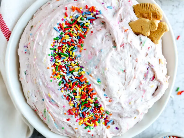 a white bowl with dunkaroo dip covered in sprinkles next to a bowl of animal crackers