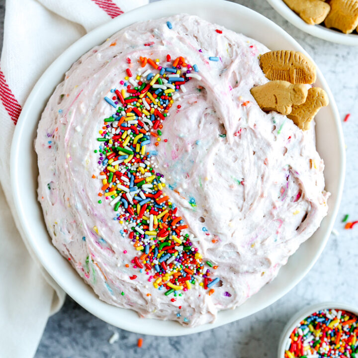 a white bowl with dunkaroo dip covered in sprinkles next to a bowl of animal crackers