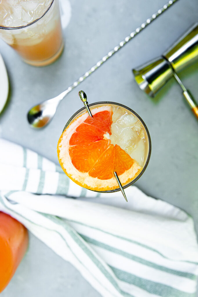 an overhead shot of a half circle of a grapefruit wedge on a cocktail glass with bar tools surrounding it