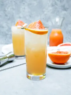 a highball glass filled with light orange grapefruit crush and a grapefruit wedge on a cocktail pick