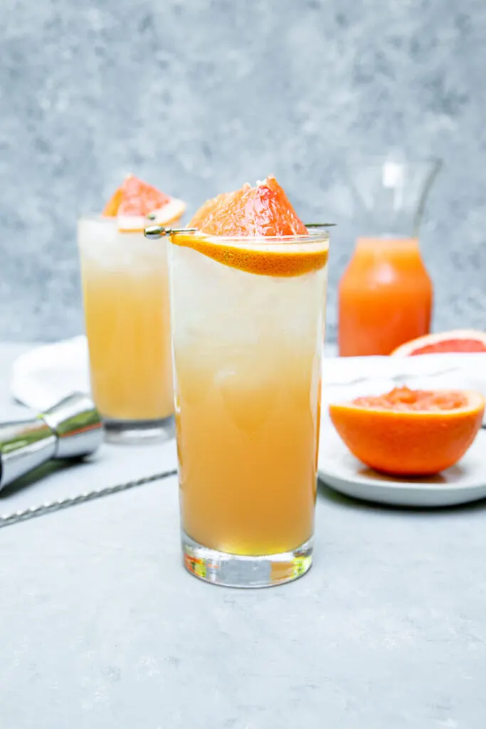 a highball glass filled with light orange grapefruit crush and a grapefruit wedge on a cocktail pick