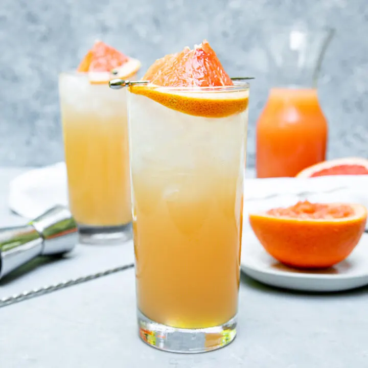 a highball glass filled with light orange grapefruit crush and a grapefruit wedge on a cocktail pick