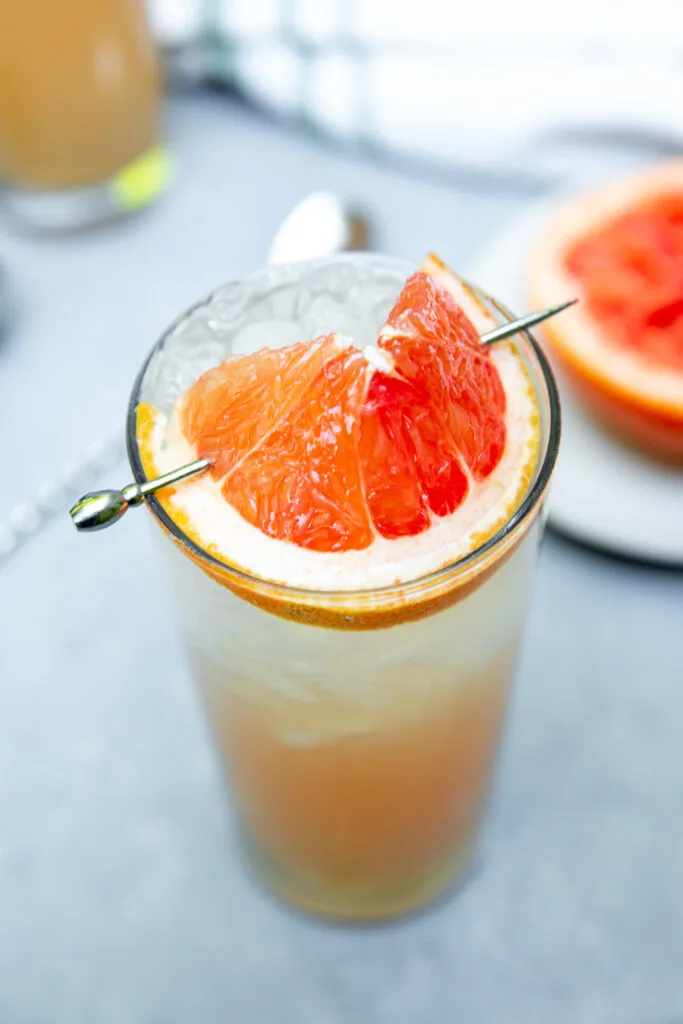 a close up of a grapefruit wedge on a metal cocktail pick on a glass