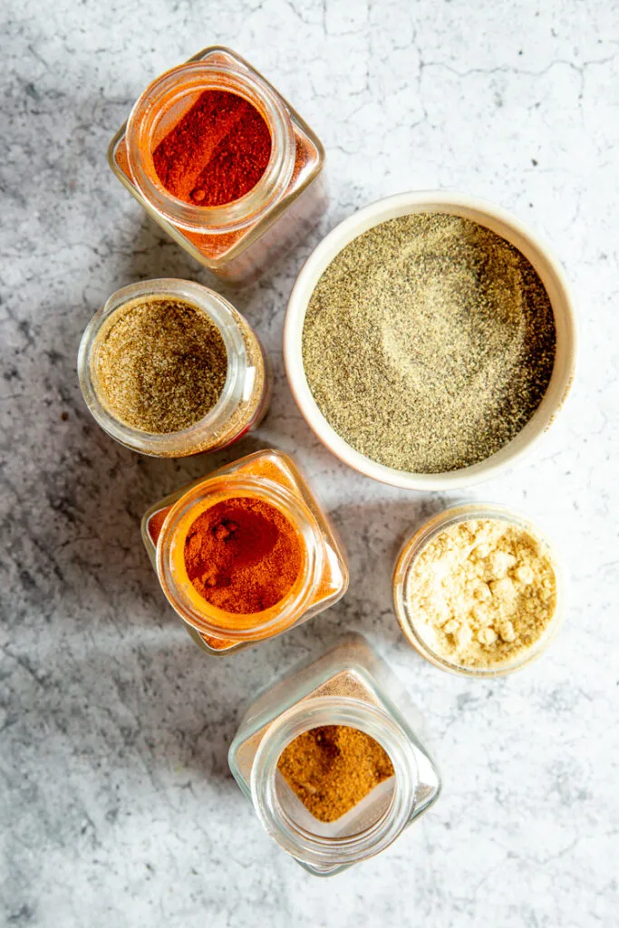 glass spice containers with celery salt, paprika, pepper, cayenne pepper, dried mustard, and nutmeg