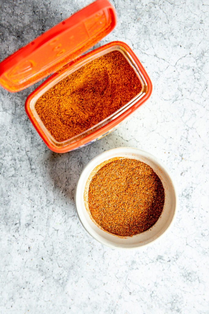 a top angle of an open container of old bay and a small bowl of old bay seasoning substitute