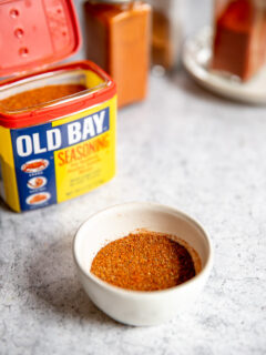 a small white bowl of old bay seasoning substitute in front of old bay and clear glass containers