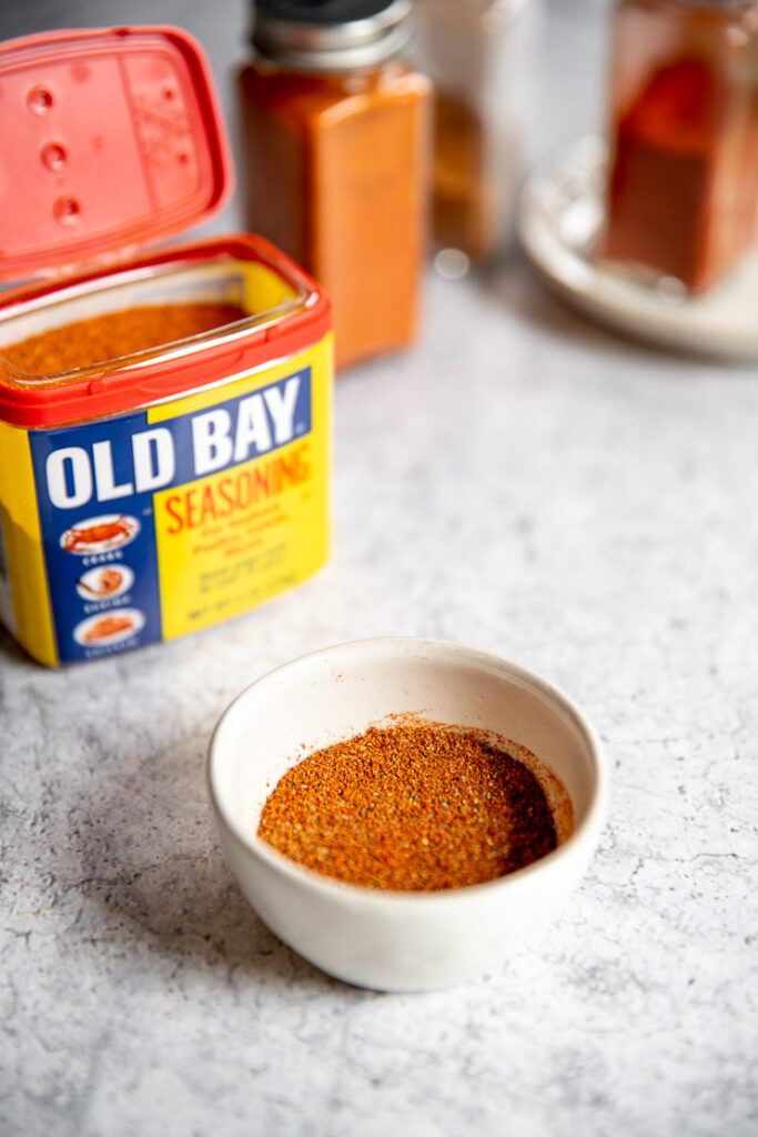 a small white bowl of old bay seasoning substitute in front of old bay and clear glass containers