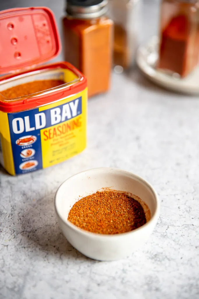 a small white bowl of old bay seasoning substitute in front of old bay and clear glass containers