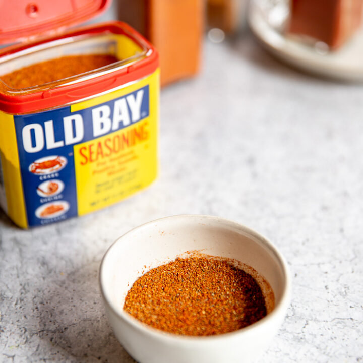 a small white bowl of old bay seasoning substitute in front of old bay and clear glass containers