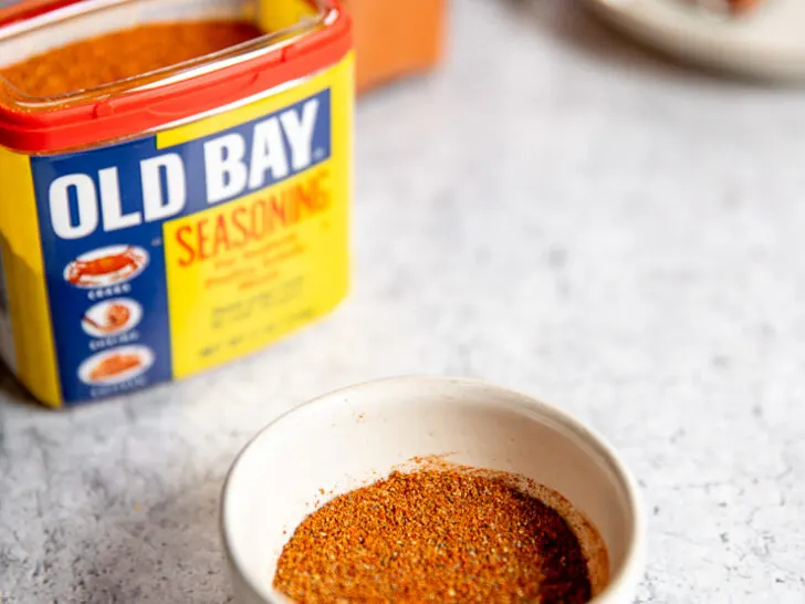 a small white bowl of old bay seasoning substitute in front of old bay and clear glass containers