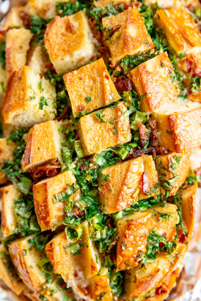 a close up of herbs and bacon peeking out of the cuts of a sourdough loaf