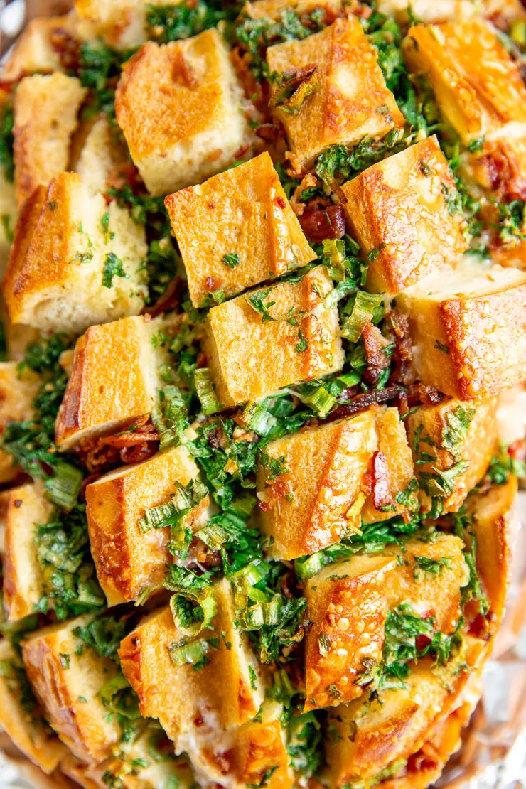 a close up of herbs and bacon peeking out of the cuts of a sourdough loaf