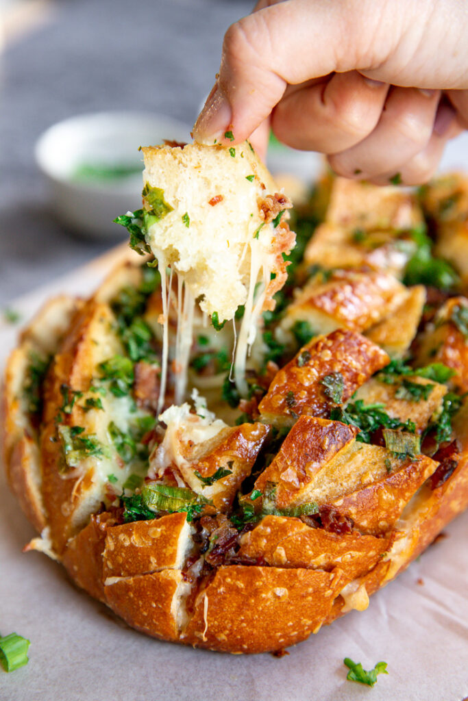 a piece of garlic bread being pulled from the loaf with a string of cheese attached