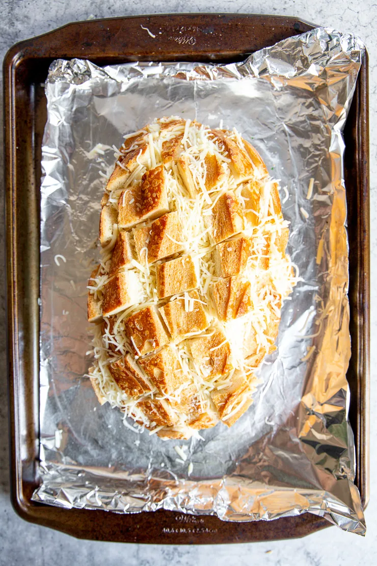 a cut loaf of sourdough bread with shredded cheese between the cuts