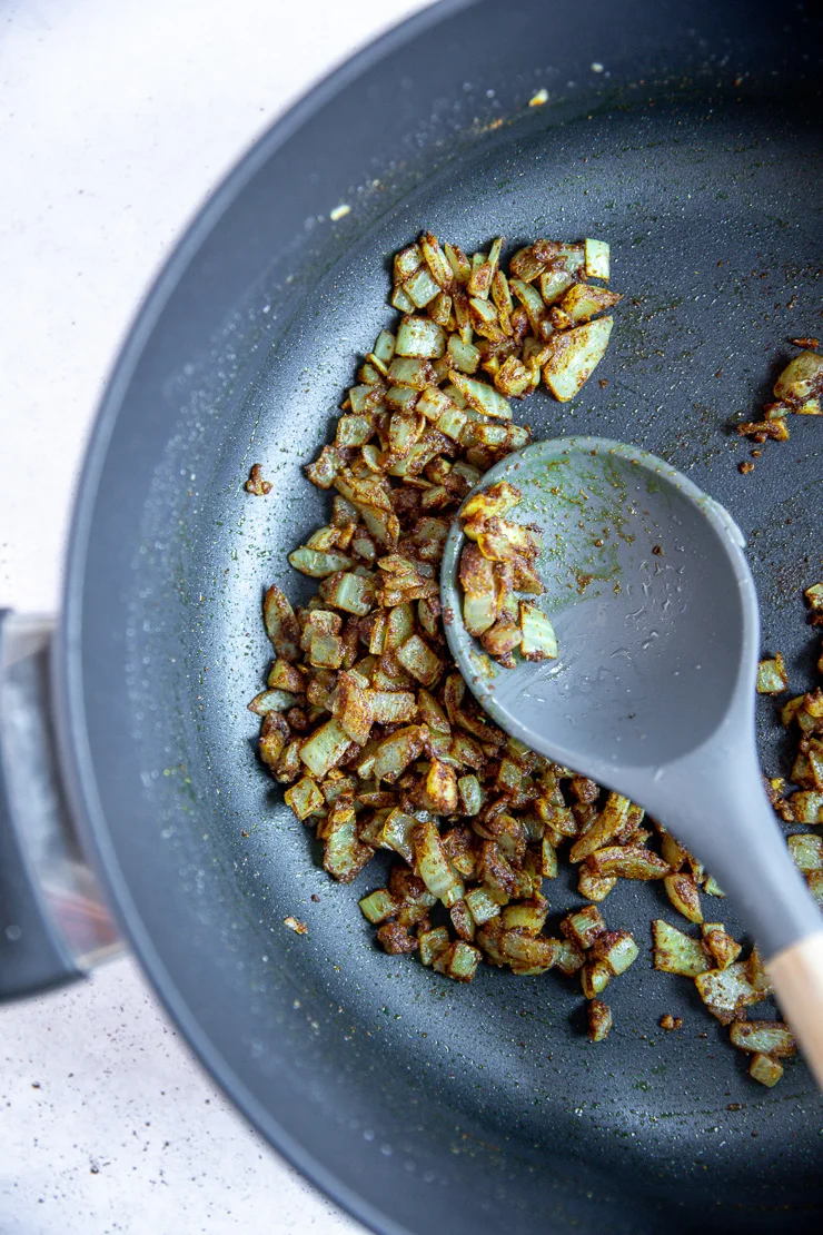 a metal pot with curry spices and diced onion with a spoon stirring