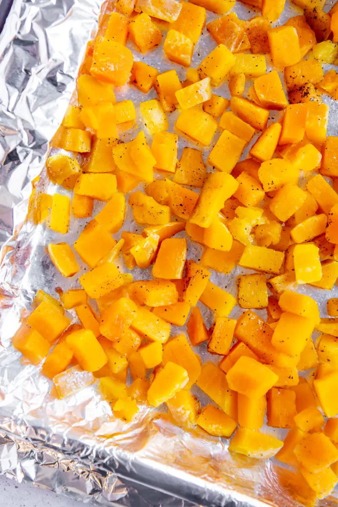 aluminum foil on a sheet pan covered with diced butternut squash seasoned with salt, pepper, and oil