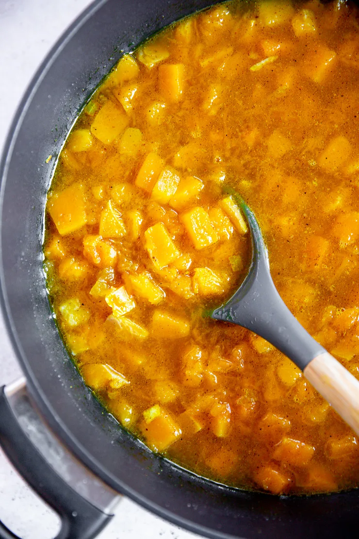 a metal pot filled with roasted butternut squash, diced onion, and vegetable broth being stirred