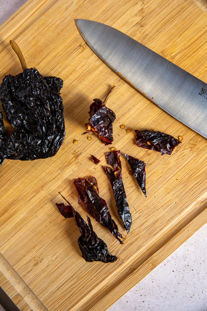 A wooden cutting board with a cut ancho chile pepper and a knife.