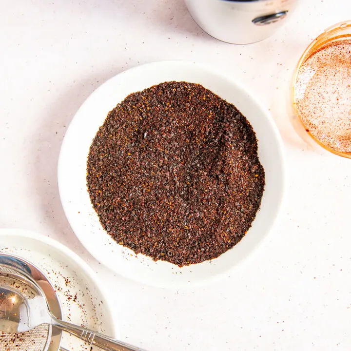 A small white plate with blended ancho chile powder next to a spice grinder and a small mesh sieve.