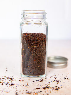 A glass spice jar filled with ancho chile powder.