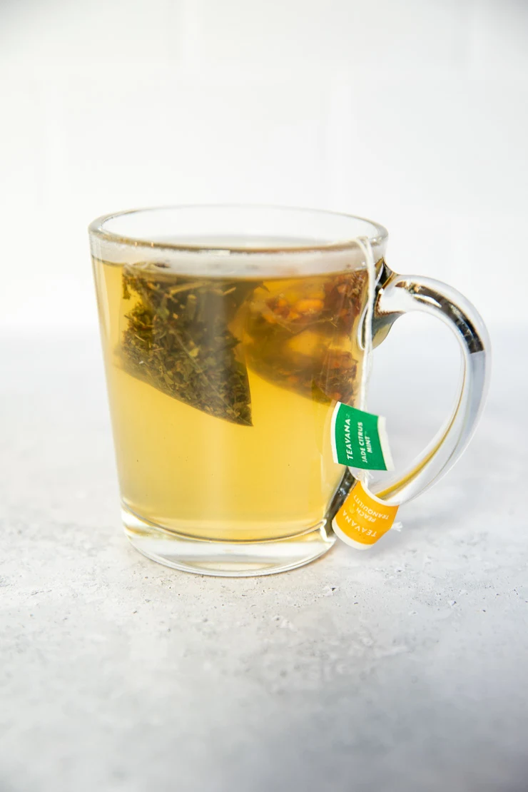 A clear glass mug with warm water and lemonade being steeped with two tea bags.