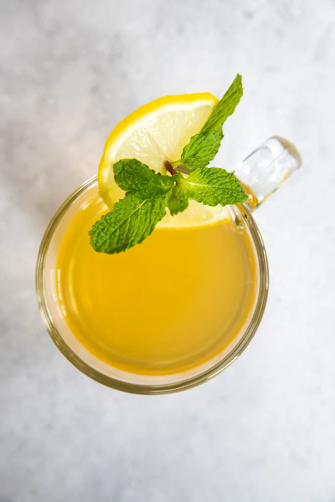 An overhead shot of a glass with tea, lemon round, and mint leaf garnish.