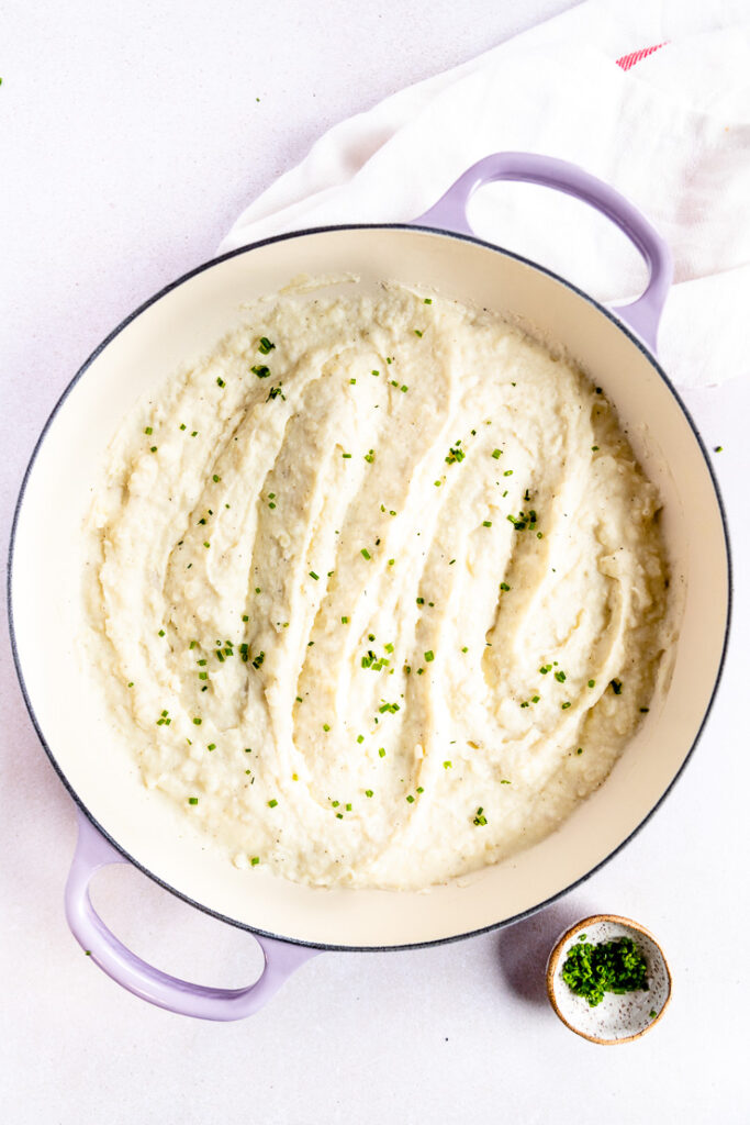 Horseradish mashed potatoes topped with diced chives in a large enameled pan.