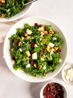 An overhead shot of the Kale Salad with Cranberries next to two small dishes of dried cranberries and goat cheese.