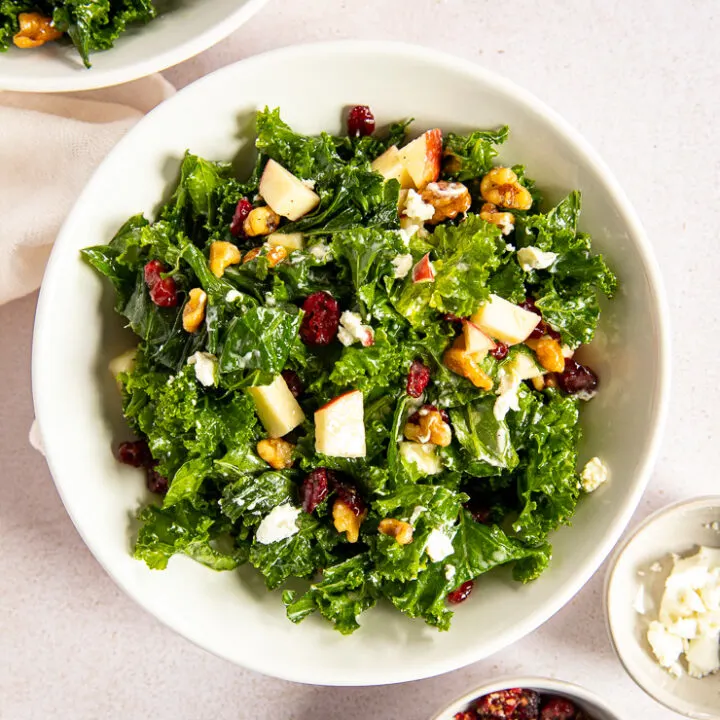 An overhead shot of the Kale Salad with Cranberries next to two small dishes of dried cranberries and goat cheese.