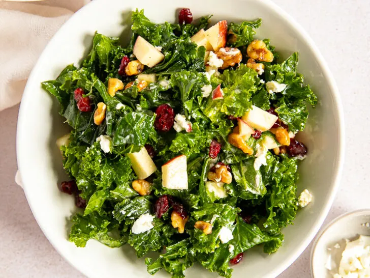 An overhead shot of the Kale Salad with Cranberries next to two small dishes of dried cranberries and goat cheese.