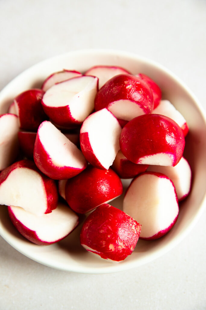 A white bowl of halves of radishes.