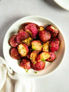 An overhead shot of a white bowl filled with halves of roasted radishes topped with diced chives.