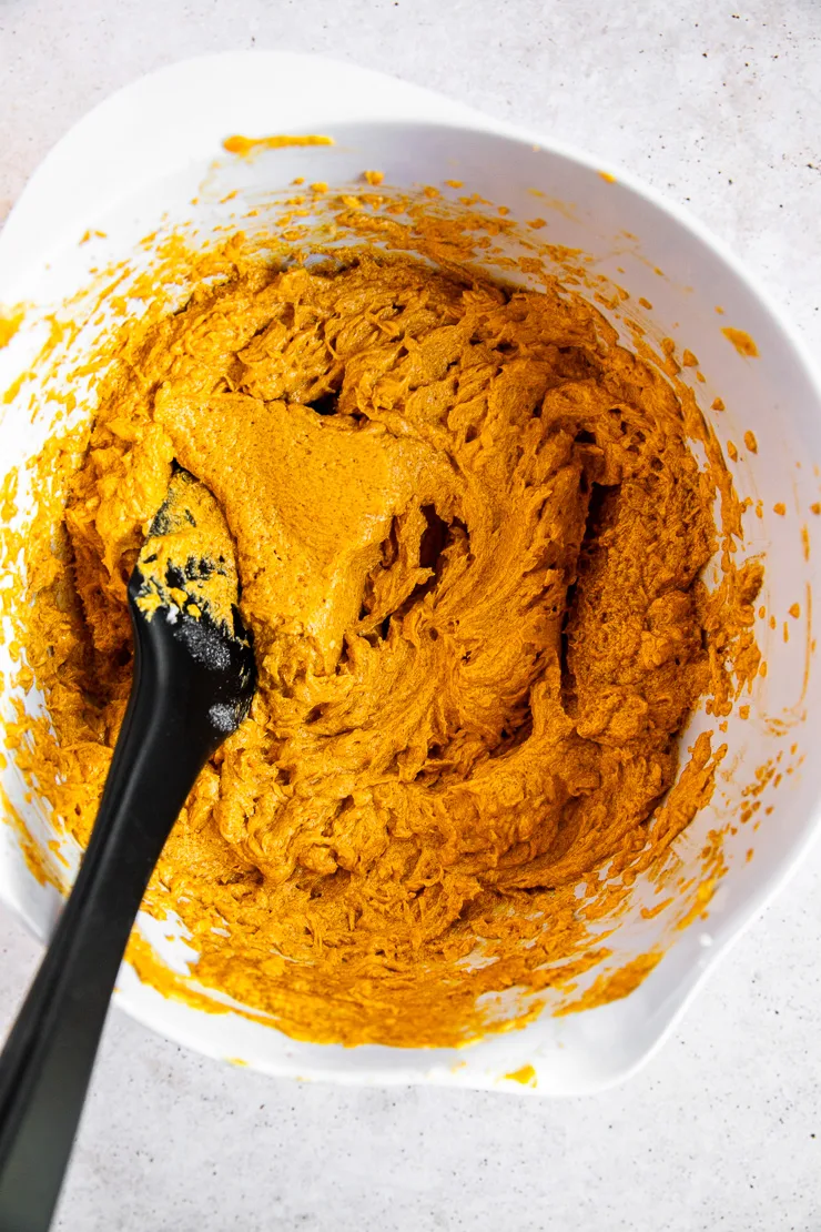 A white bowl and black spatula stirring pumpkin cookie dough.