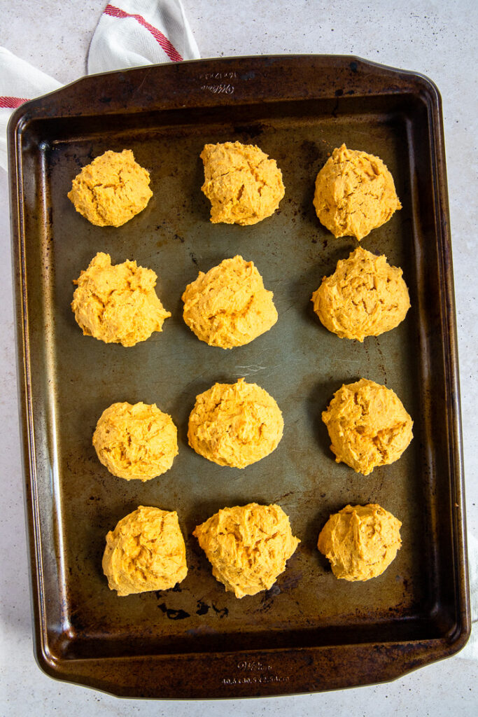 An aged cookie sheet with 12 baked pumpkin cookies resting on a linen napkin.