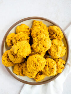 An overhead shot of a pile of soft pumpkin cookies on a plate with a brown rim on a white linen napkin.