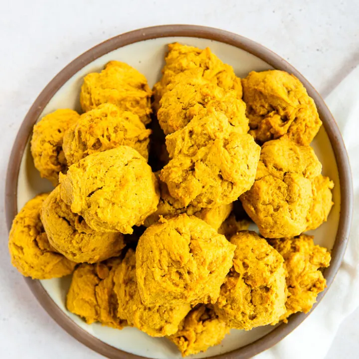 An overhead shot of a pile of soft pumpkin cookies on a plate with a brown rim on a white linen napkin.