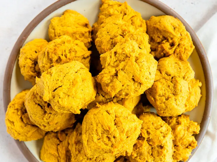 An overhead shot of a pile of soft pumpkin cookies on a plate with a brown rim on a white linen napkin.