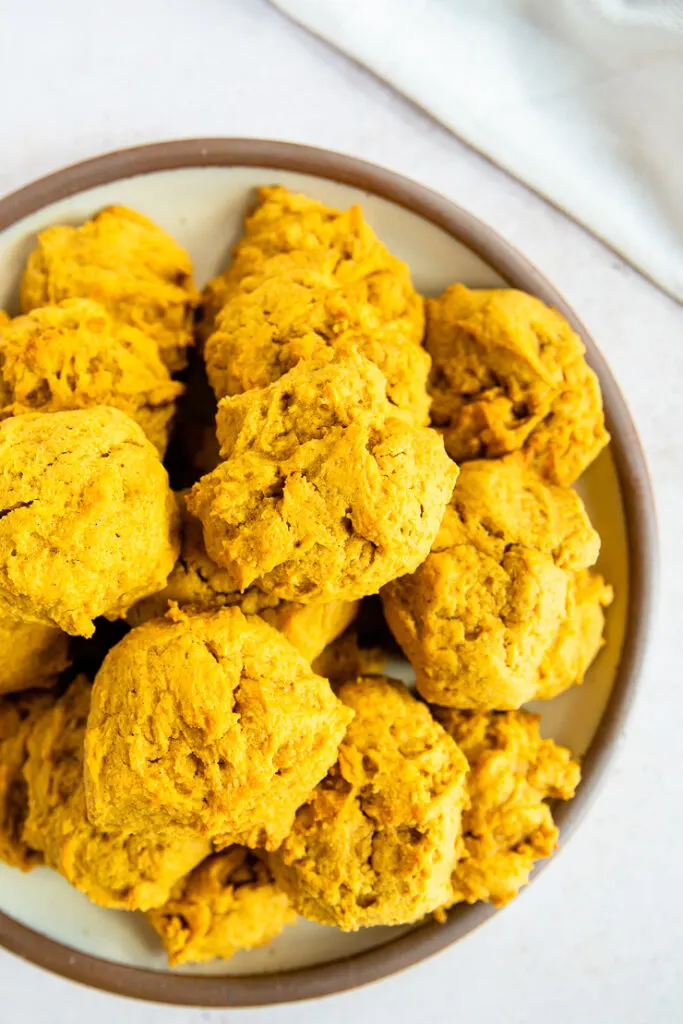 A close up of crinkly orange pumpkin cookies in a pile on a plate.