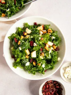 An overhead shot of the Kale Salad with Cranberries next to two small dishes of dried cranberries and goat cheese.
