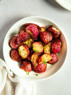 An overhead shot of a white bowl filled with halves of roasted radishes topped with diced chives.