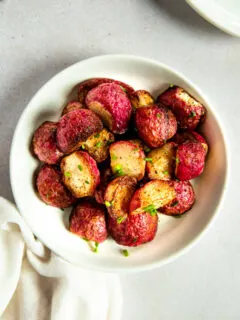 An overhead shot of a white bowl filled with halves of roasted radishes topped with diced chives.