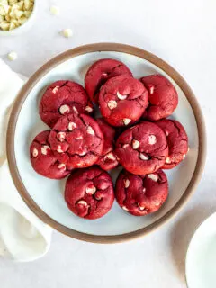 A white plate with a brown edge piled with Red Velvet Cake Mix Cookies with white chocolate chips in them.