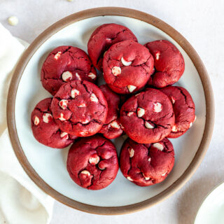 A white plate with a brown edge piled with Red Velvet Cake Mix Cookies with white chocolate chips in them.