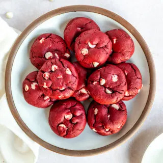 A white plate with a brown edge piled with Red Velvet Cake Mix Cookies with white chocolate chips in them.