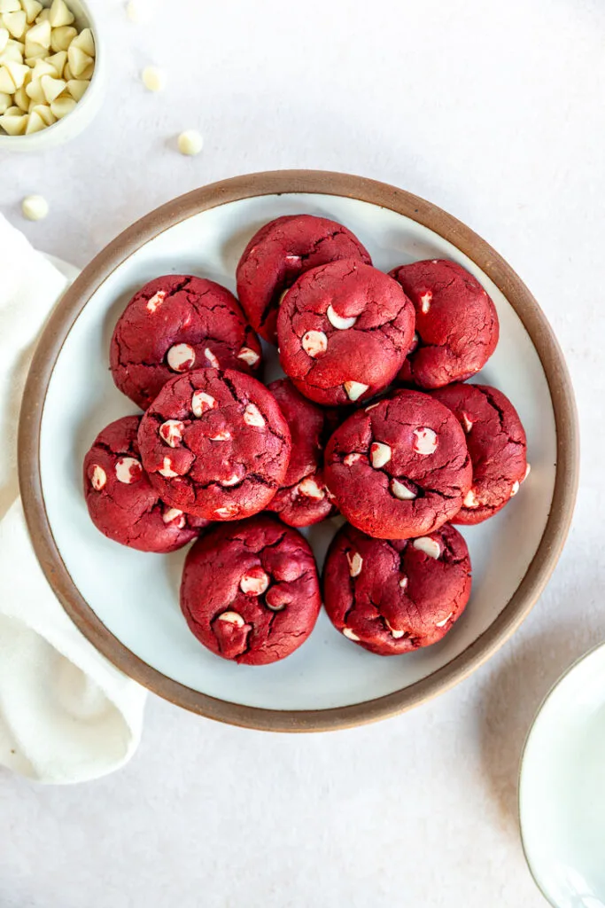 A white plate with a brown edge piled with Red Velvet Cake Mix Cookies with white chocolate chips in them.