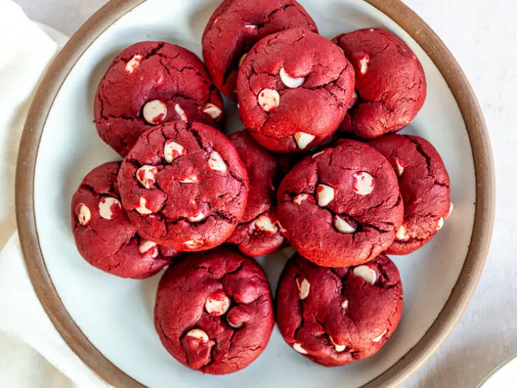 A white plate with a brown edge piled with Red Velvet Cake Mix Cookies with white chocolate chips in them.