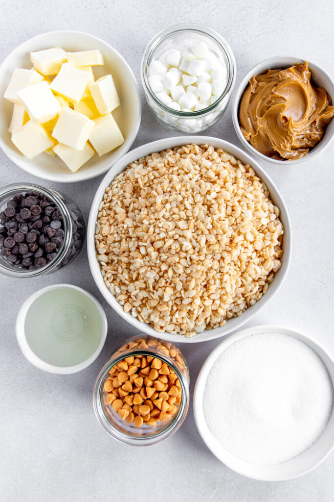 Eight different bowls of varying sizes and shades of white and clear filled with the ingredients needed to make scotcharoos.